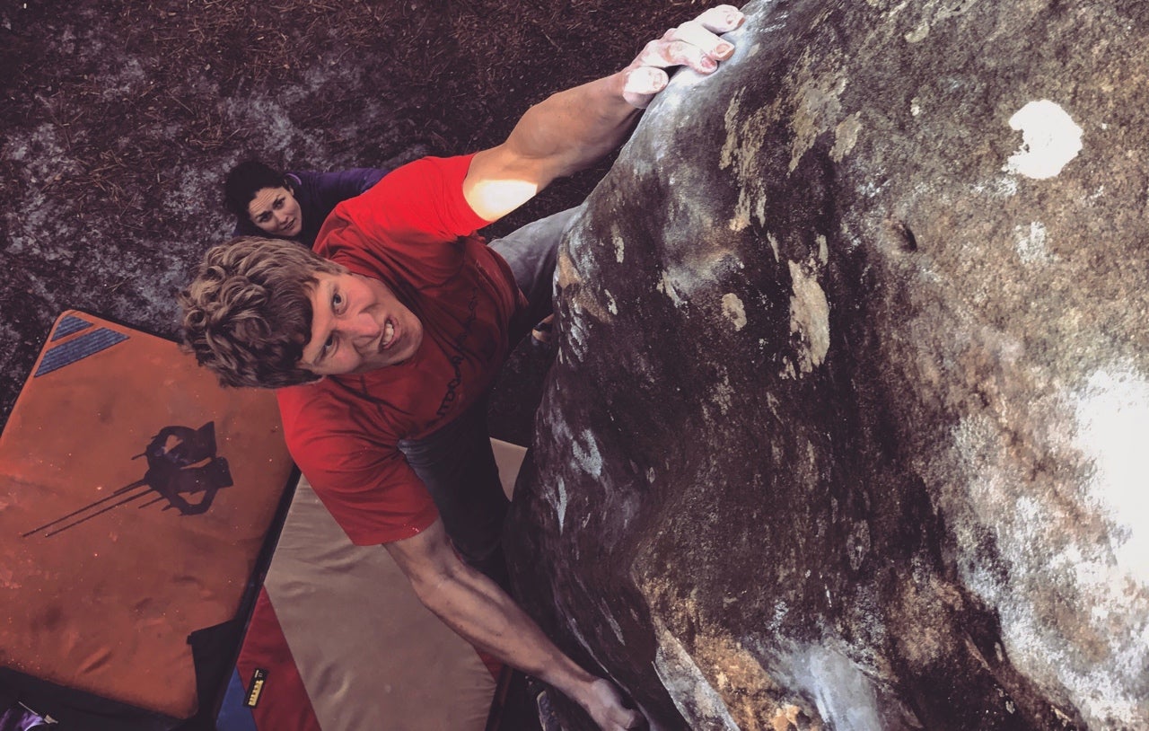 Climber in red t-shirt climbs a gray rock. A strong hand grabbed