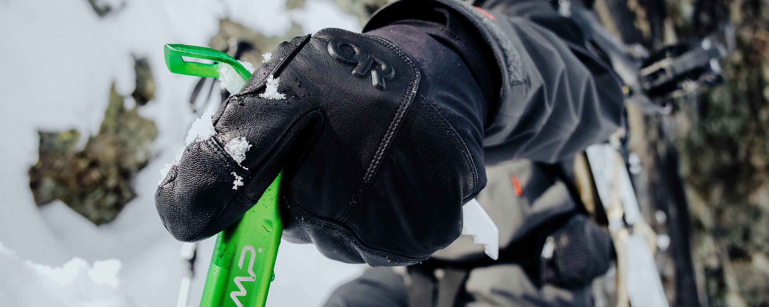 Athlete Max Djenohan climbs a mountain while gripping a Pickaxe with the Outdoor Research Team Gore-Tex 3-Finger Gloves in Black. 