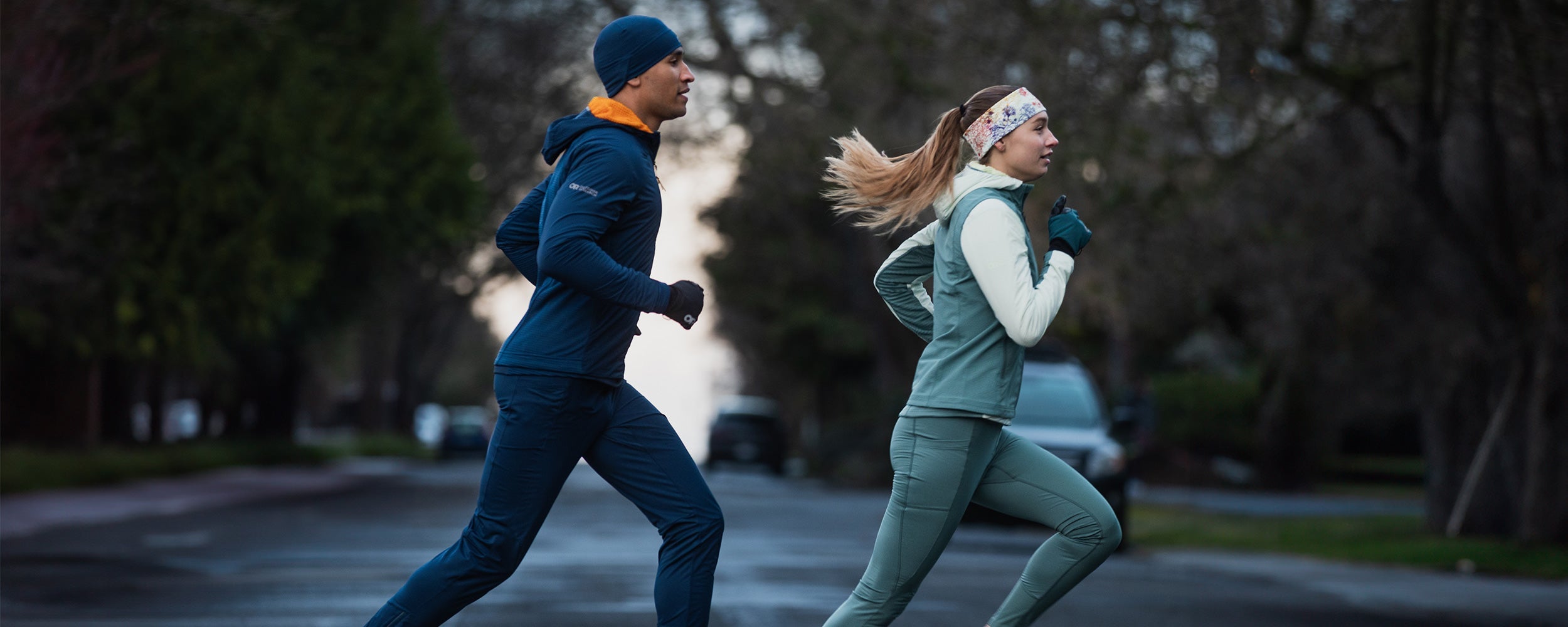 Two runners jog across the crosswalk wearing Outdoor Research Sportswear. 