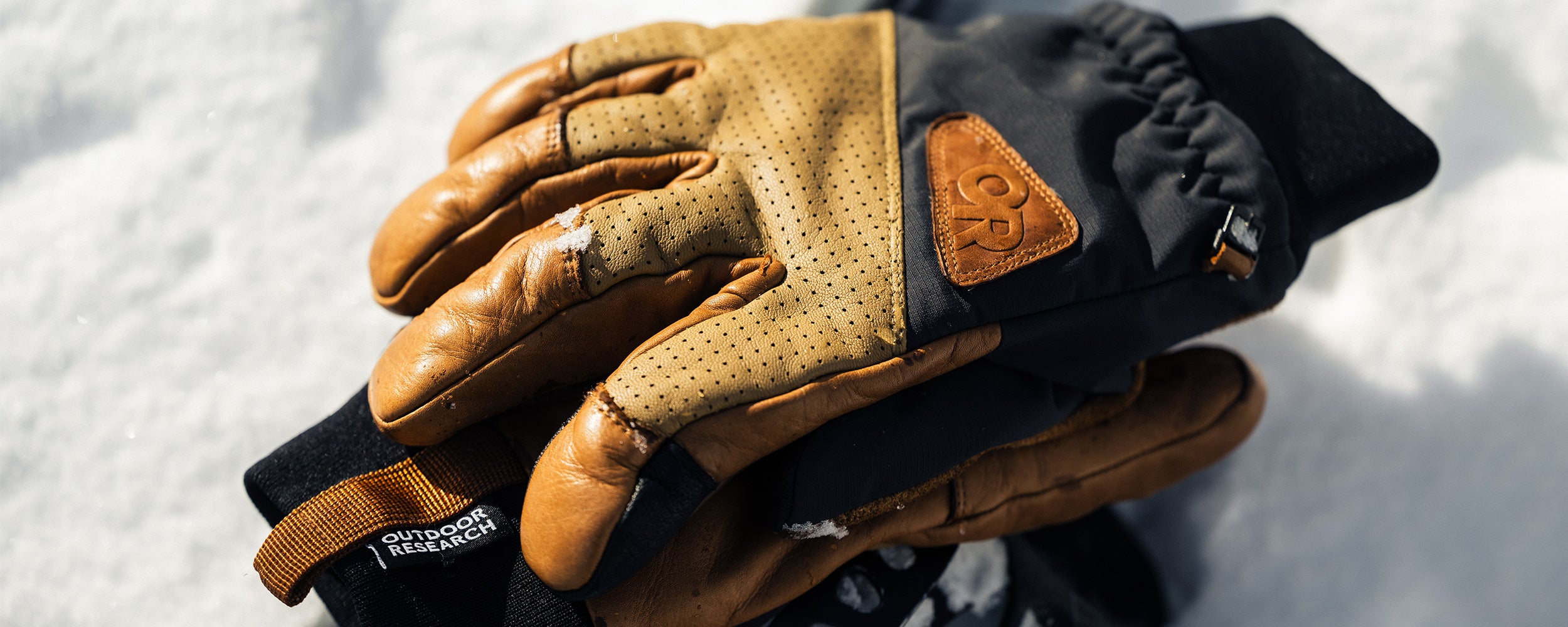 A pair of Outdoor Research Snowcrew Leather Gloves in Dark Natural/Black rest on the snow.