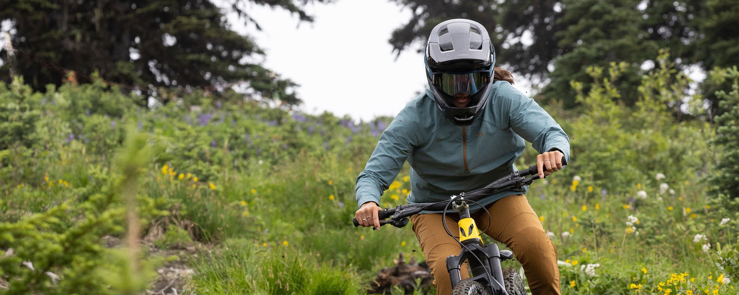 Outdoor Research mountain bike athlete Georgia Astle rides down a trail wearing the Freewheel Half Zip Soft Shell MTB Hoodie. 