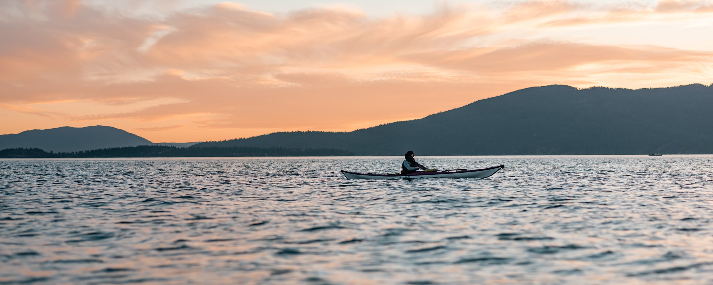 A woman paddles her sea kayak at sunset.