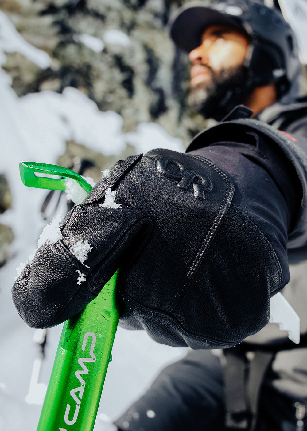 Athlete Max Djenohan climbs a mountain while gripping a Pickaxe with the Outdoor Research Team Gore-Tex 3-Finger Gloves in Black. 