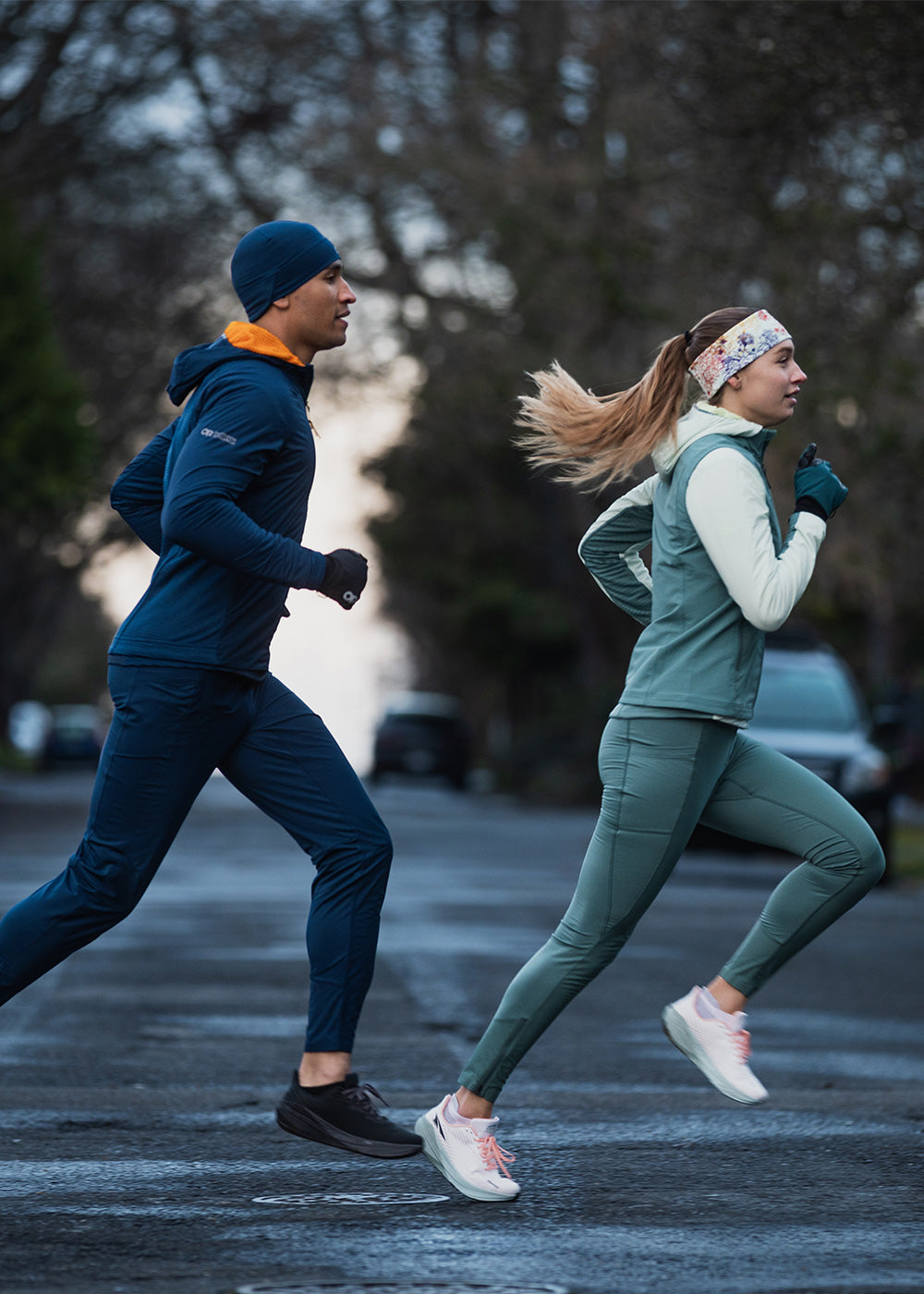 Two runners jog across the crosswalk wearing Outdoor Research Sportswear. 