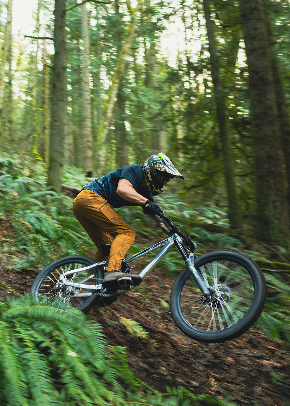 Man bikes downhill in forest while wearing the Outdoor Research Freewheel Mountain Bike Collection. 