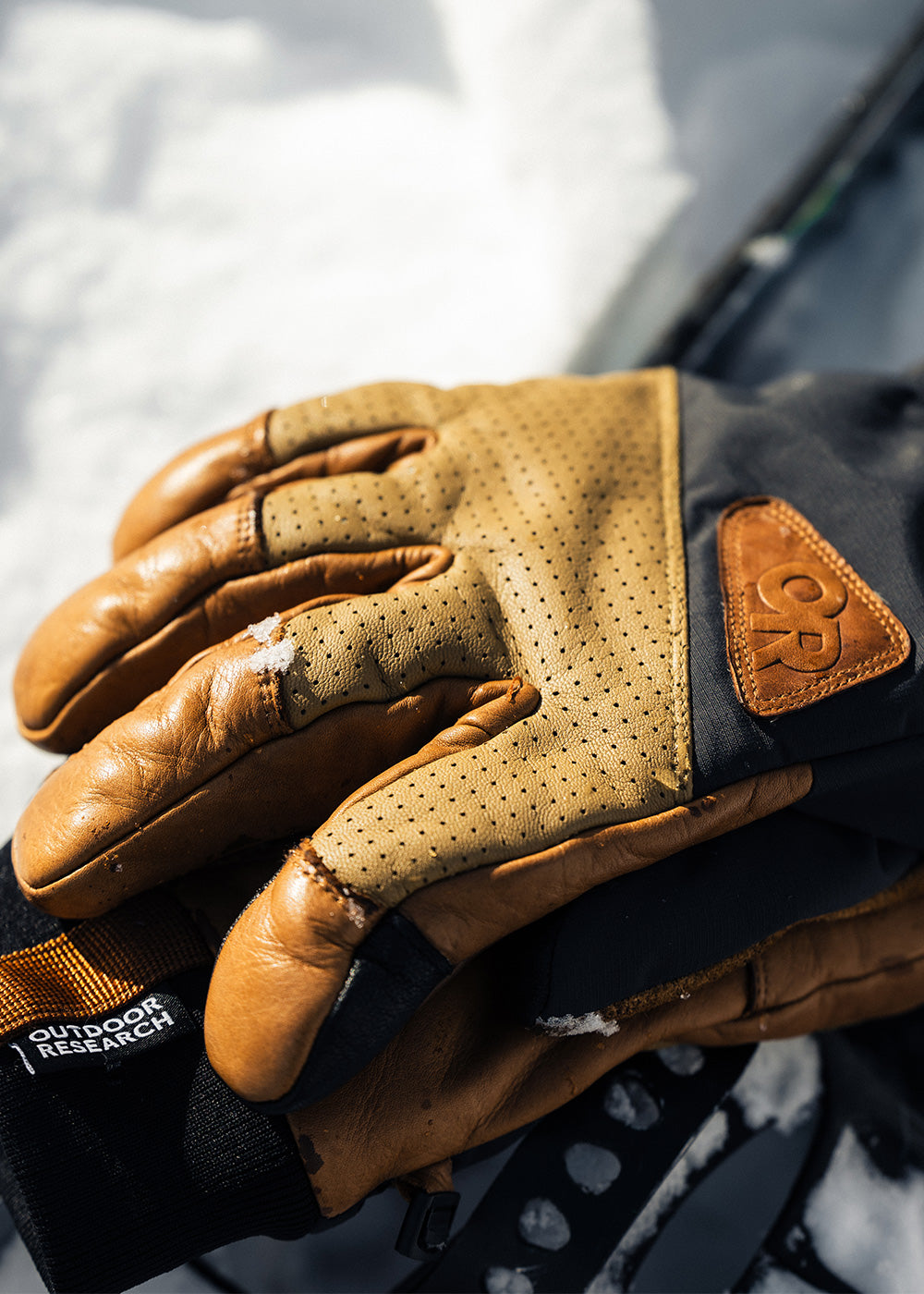 A pair of Outdoor Research Snowcrew Leather Gloves in Dark Natural/Black rest on the snow.