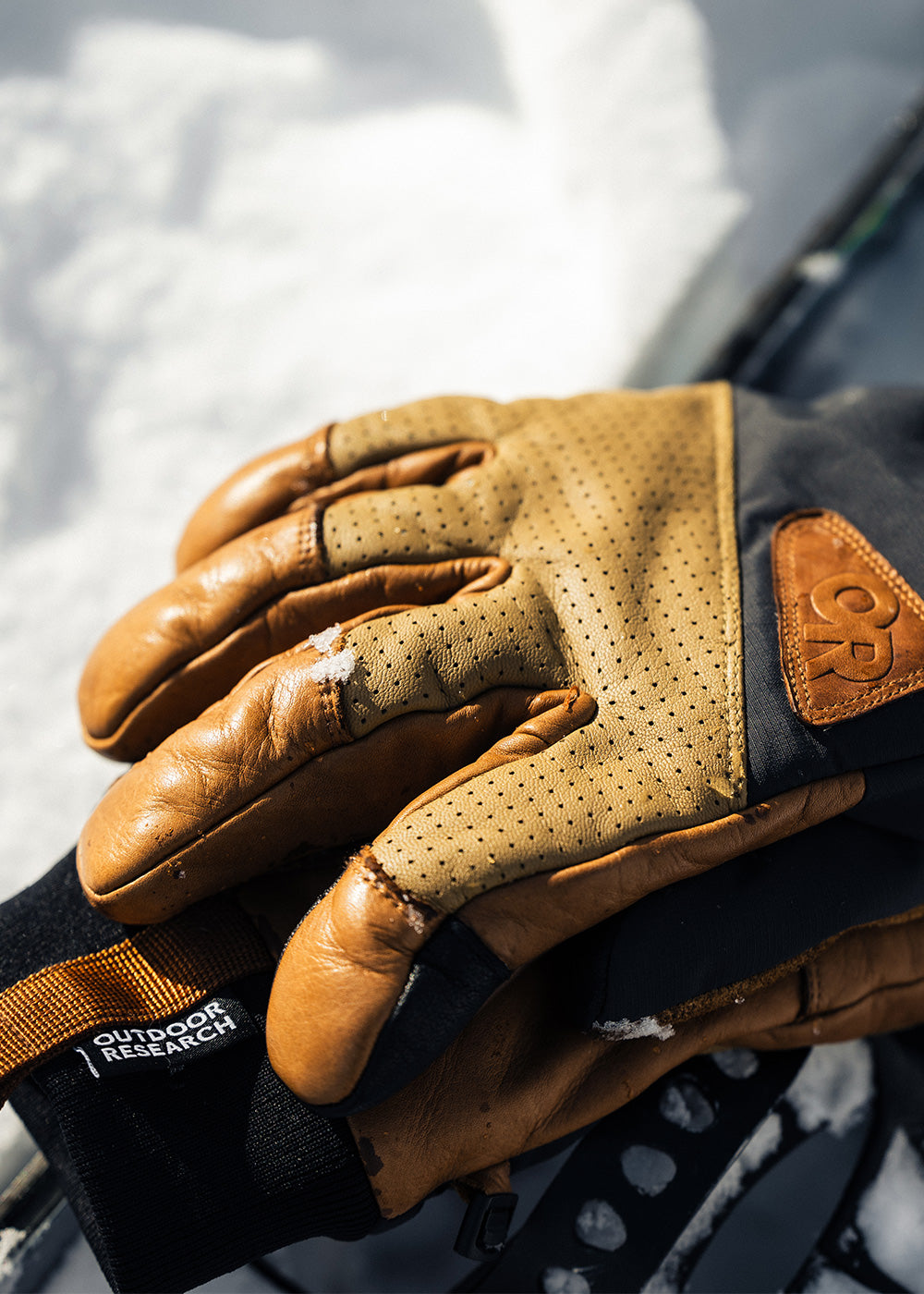 A pair of Outdoor Research Snowcrew Leather Gloves in Dark Natural/Black rest on the snow.