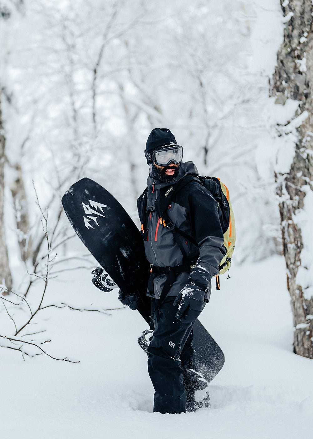 A snowboarder stays warms as he walks through the snowy forest in the Men's Headwall Gore-Tex 3L Jacket in Storm/Black.