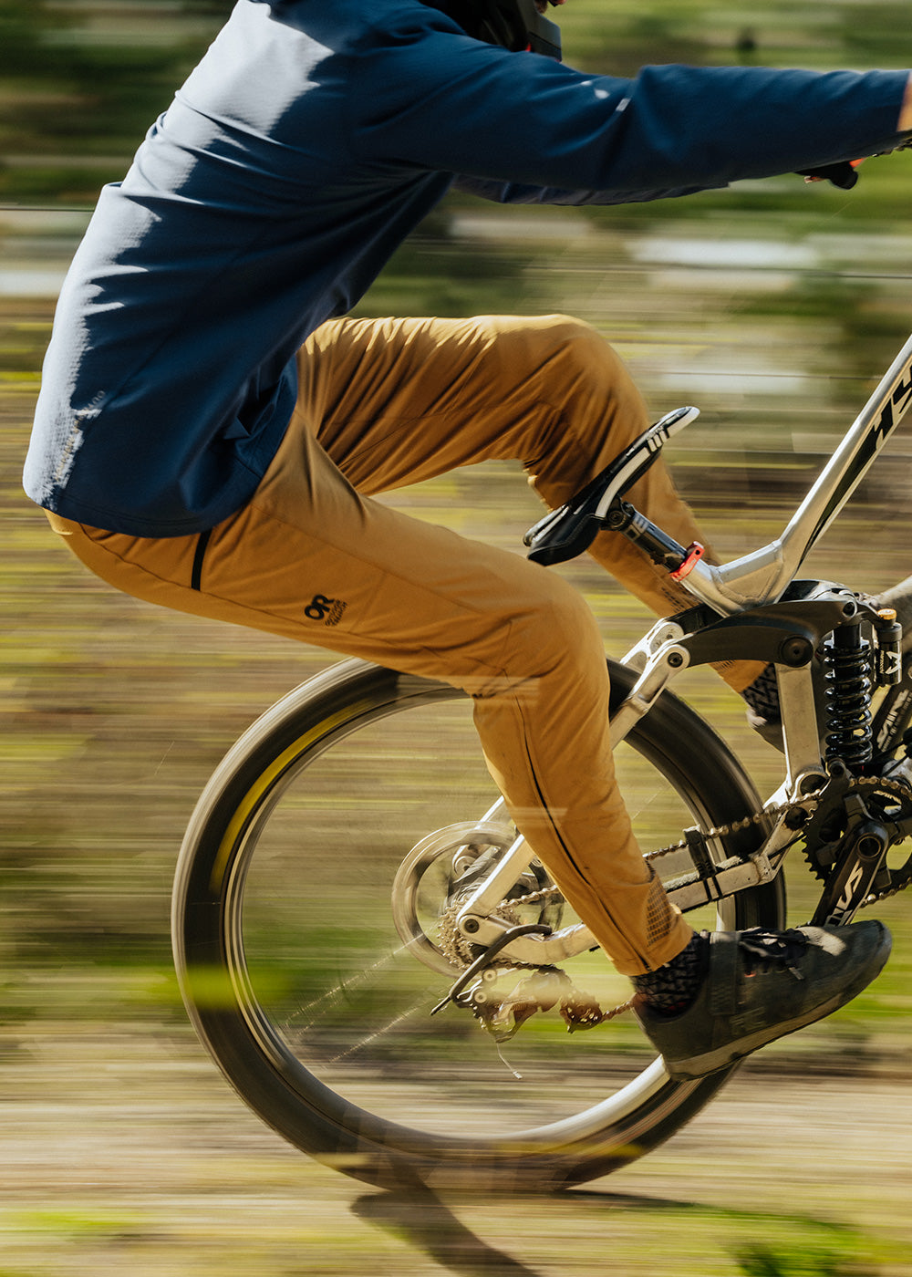 Man does a trick on his mountain bike while wearing the Freewheel Ride Pants in Bronze.