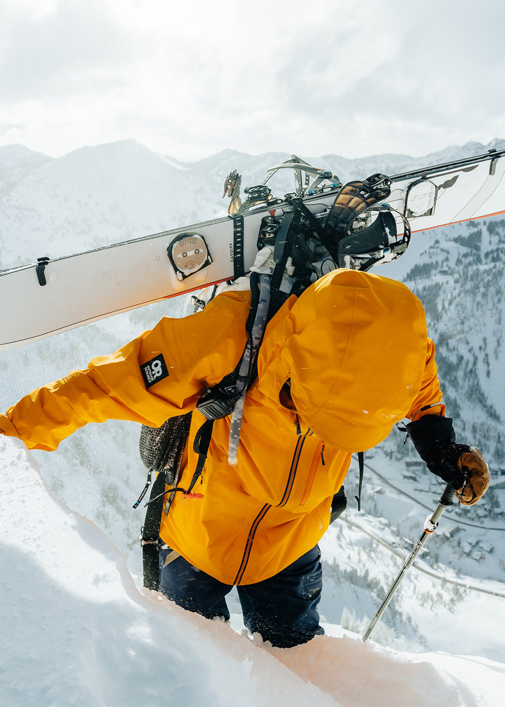 Man wearing the Outdoor Research Hemispheres ll Jacket in Gold Nebula prepares to ski at the top of the mountain. 