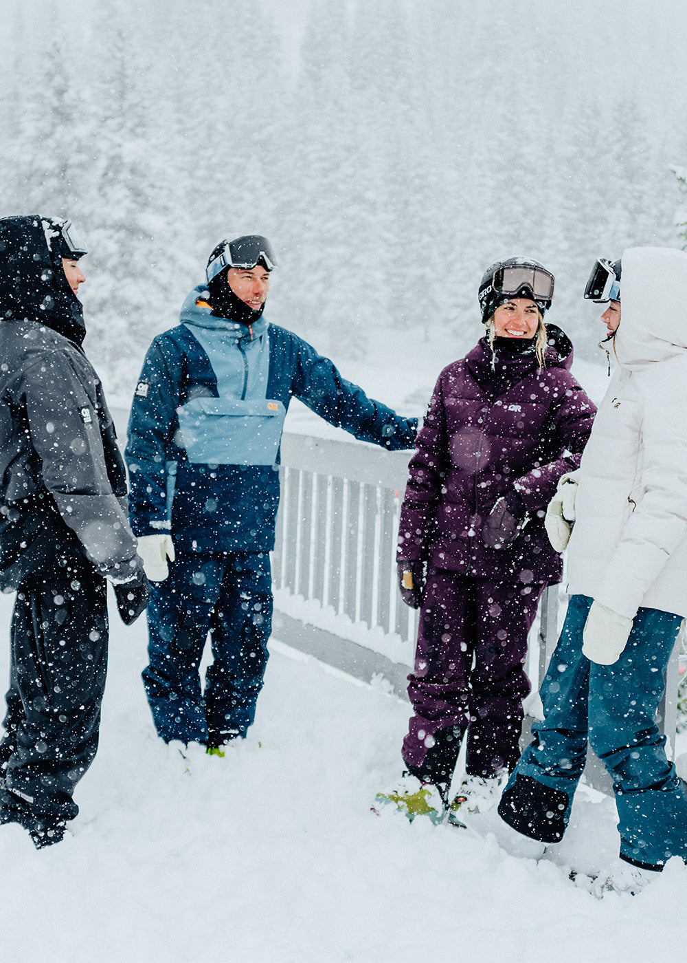 A group of four friends wearing Outdoor Research ski outerwear talk in the snow outside a lodge. 