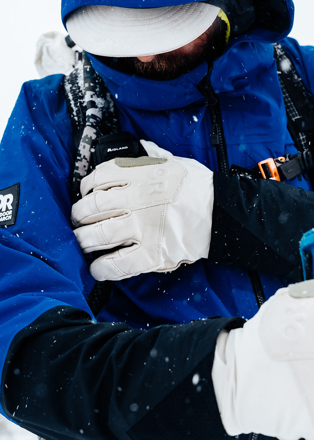 Man adjusts straps on his backpack in the snow while wearing Outdoor Research Team Gore-Tex Gloves in Oyster/Natural. 