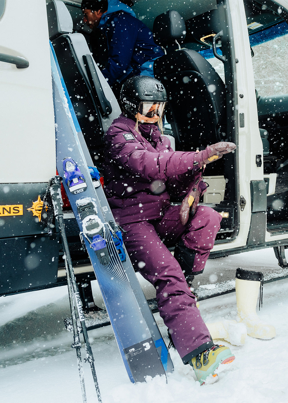 Two Females sit outside their Van in the snow to gear up in their Outdoor Research ski Outerwear. 