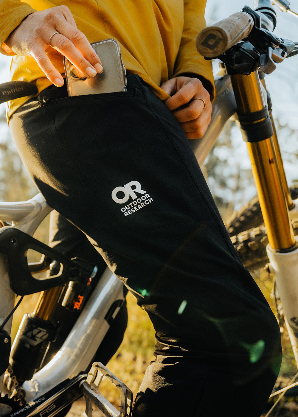 A woman puts her phone in the pocket of her Freewheel MTB Ride Pants in Black while out on a ride.