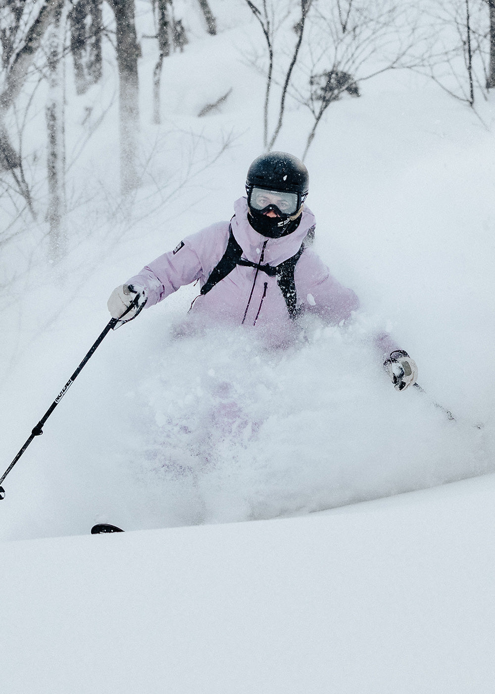 A woman skis through powder wearing the Hemispheres II Jacket in Stardust - lavender.