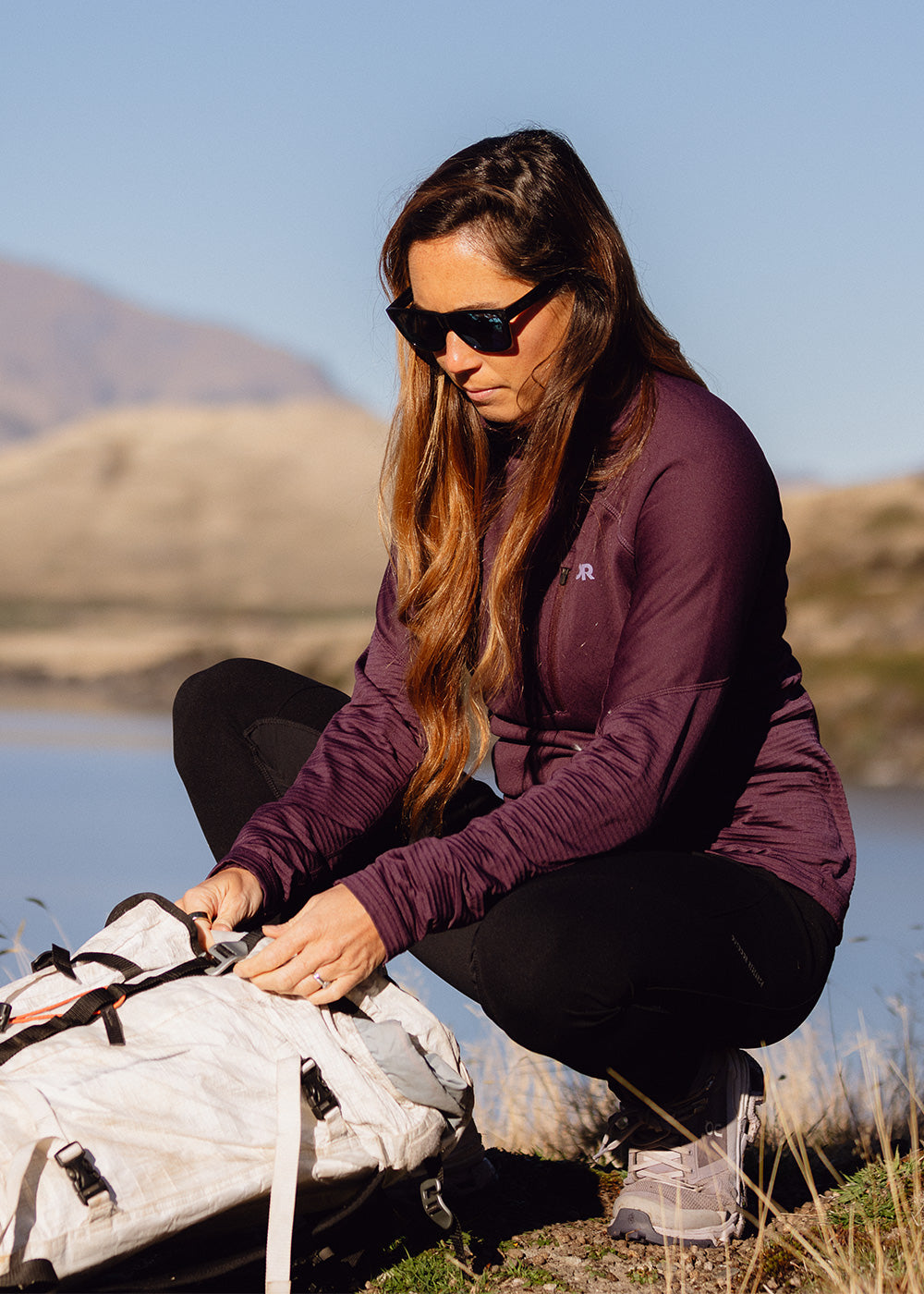 A woman wearing Outdoor Research outerwear stops during her hike to organize the gear inside her backpack. 