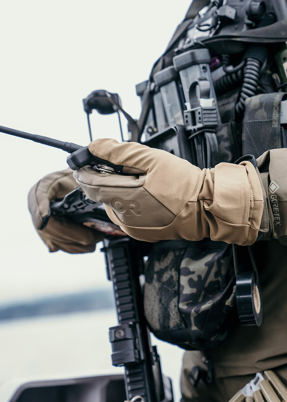 Close up of a person wearing leather gloves by Outdoor Research while holding a walkie talkie.