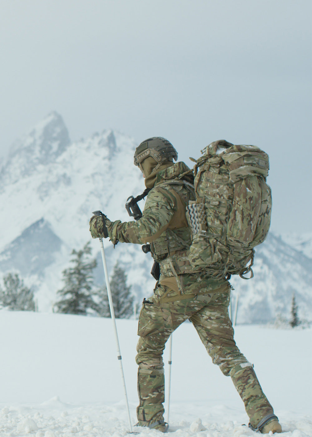 Two skiers in tactical gear cross a snowy field.