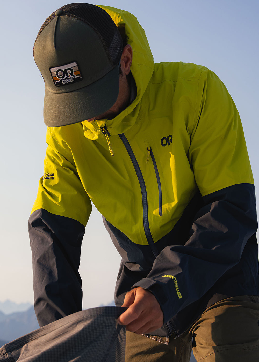 Man digs through his backpack while wearing the Outdoor Research Advocate Trucker Hi Pro Cap.