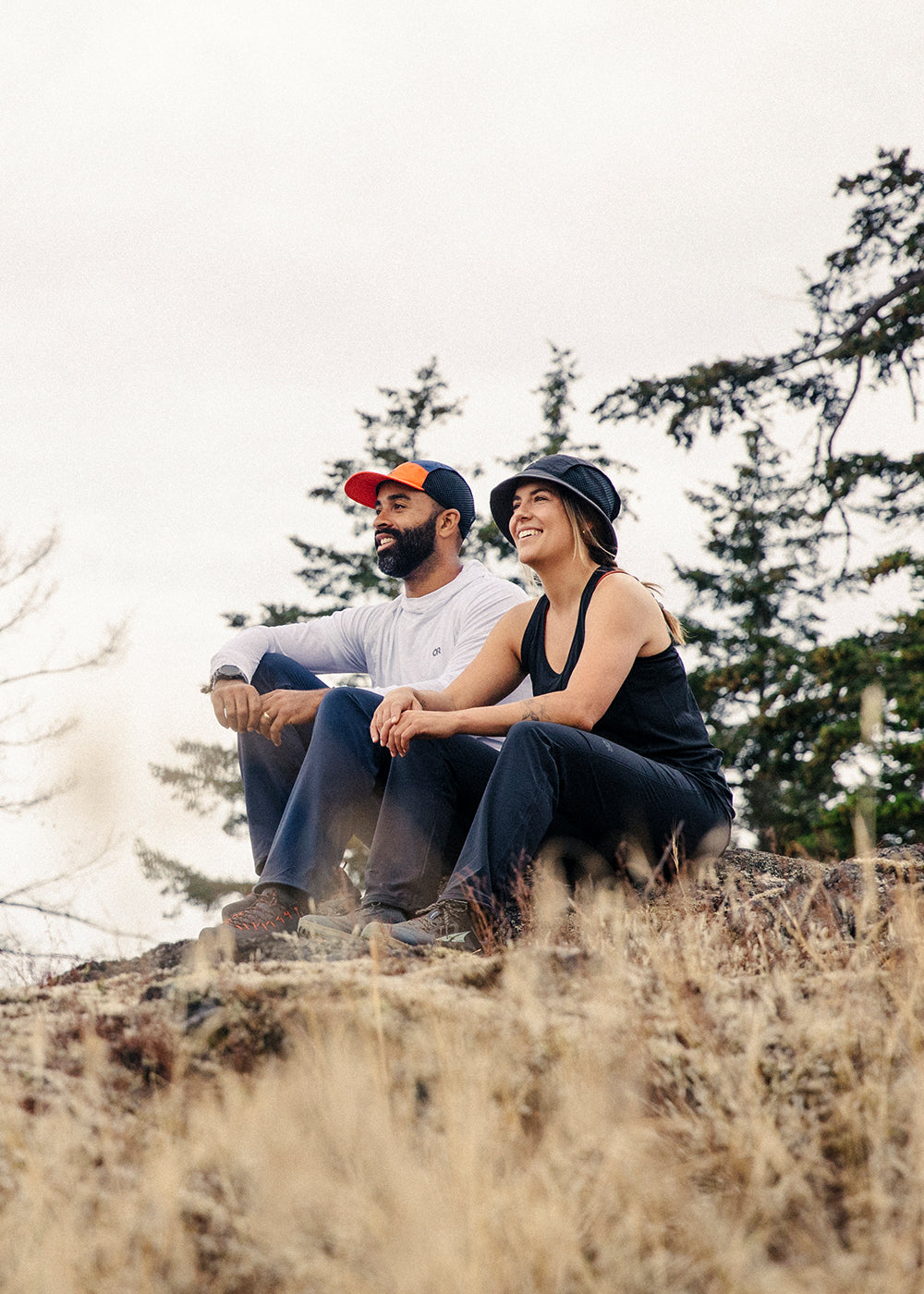 Two friends sit on a rock and enjoy the view after their hike while wearing Outdoor Research Sportwear. 