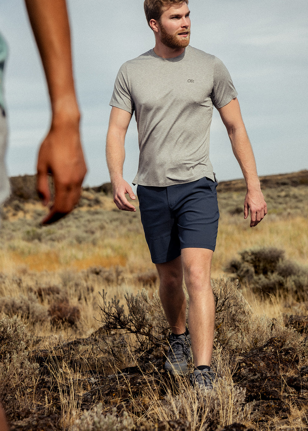 Two friends stride through a dry field under the sun wearing Outdoor Research Sportswear. 