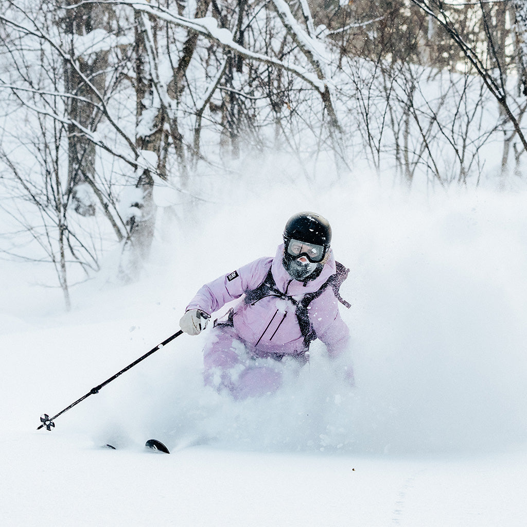 Woman wearing the Hemispheres ll Jacket in Stardust light pink skies fast down a mountain in deep snow. 