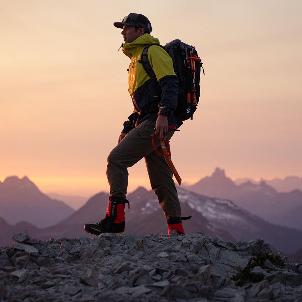 Man stands on the top of a rock watching the sunset while wearing Outdoor Research outerwear. 